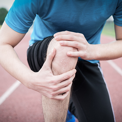 man holding knee on running track in pain